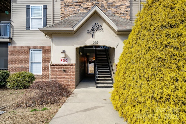 view of exterior entry with stone siding, a shingled roof, and brick siding