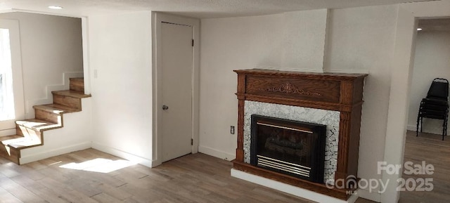 unfurnished living room with light wood-type flooring, a high end fireplace, baseboards, and stairs