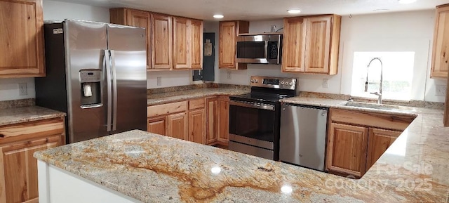 kitchen with recessed lighting, appliances with stainless steel finishes, a sink, light stone countertops, and a peninsula