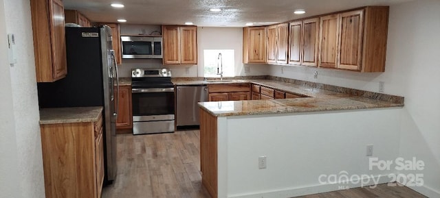 kitchen featuring brown cabinets, appliances with stainless steel finishes, a sink, light wood-type flooring, and a peninsula