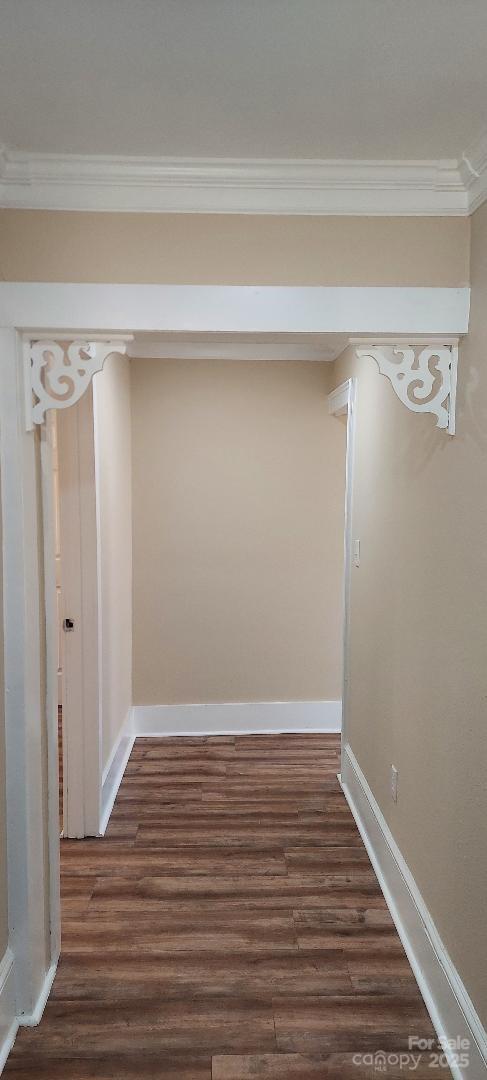 hallway featuring dark wood-type flooring, ornamental molding, and baseboards