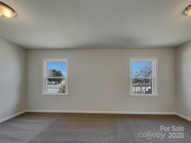 spare room with a healthy amount of sunlight, baseboards, and dark carpet