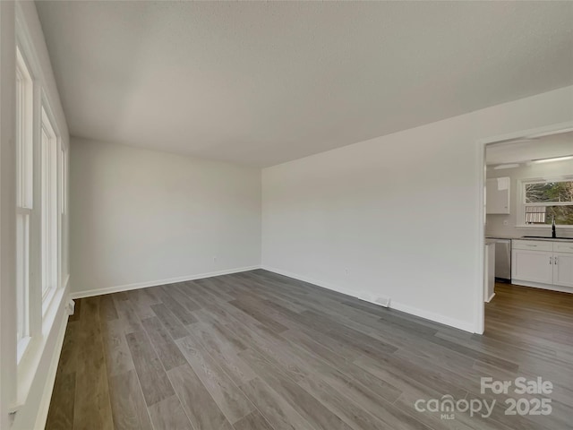 spare room featuring dark wood-style flooring, a sink, and baseboards