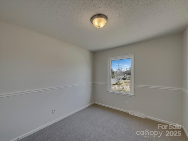 spare room with a textured ceiling, carpet, visible vents, and baseboards