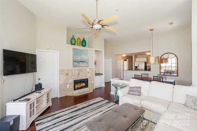 living area featuring dark wood-type flooring, vaulted ceiling, a fireplace, and ceiling fan