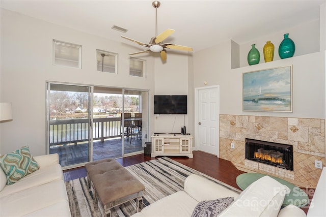 living area featuring visible vents, a high ceiling, ceiling fan, wood finished floors, and a tile fireplace