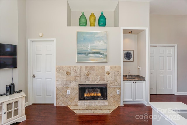 living room with a tiled fireplace, baseboards, indoor wet bar, and dark wood-style flooring