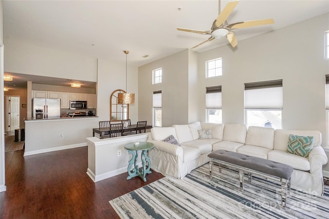 living area featuring dark wood-style flooring, baseboards, ceiling fan, and a high ceiling