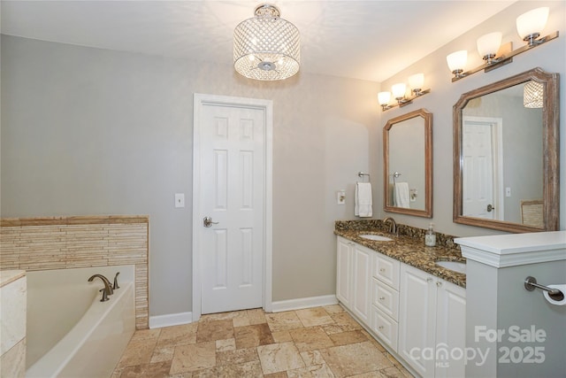 bathroom featuring double vanity, stone tile floors, baseboards, a tub, and a sink