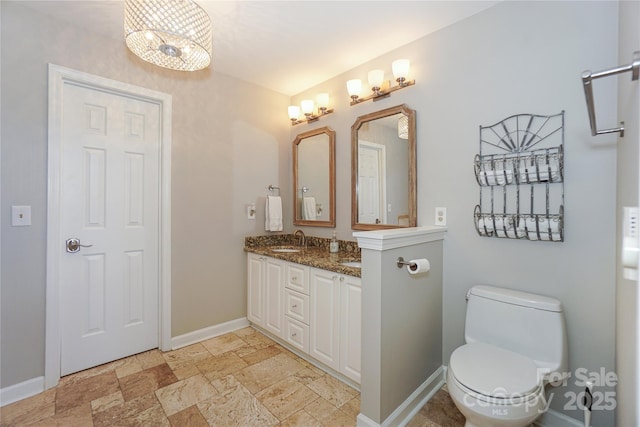 bathroom with double vanity, baseboards, toilet, stone tile flooring, and a sink