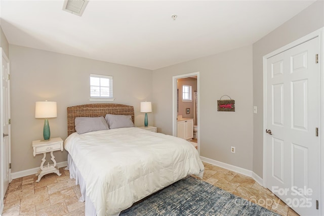 bedroom with stone tile flooring, visible vents, baseboards, and ensuite bathroom