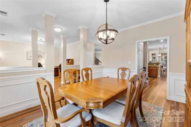 dining area with light wood finished floors, a wainscoted wall, crown molding, and decorative columns