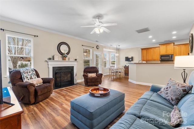 living area with light wood finished floors, a fireplace with flush hearth, crown molding, and visible vents