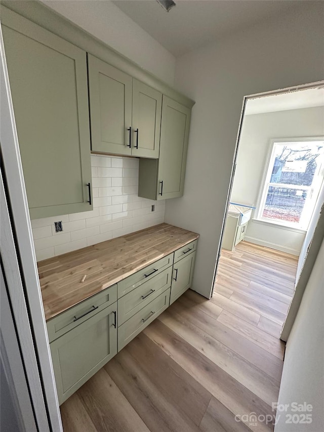 kitchen with light wood-type flooring, butcher block counters, green cabinetry, and backsplash