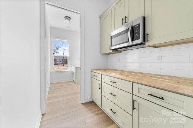 kitchen with light wood finished floors, tasteful backsplash, stainless steel microwave, butcher block countertops, and baseboards