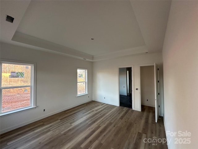 empty room featuring baseboards, a raised ceiling, and dark wood-style flooring