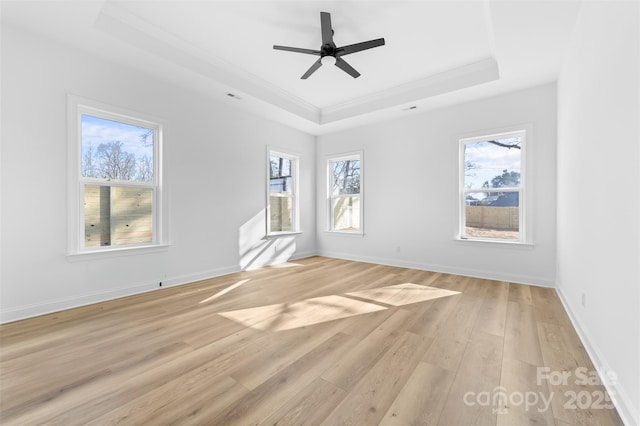 unfurnished room featuring light wood-style floors, a tray ceiling, crown molding, and baseboards