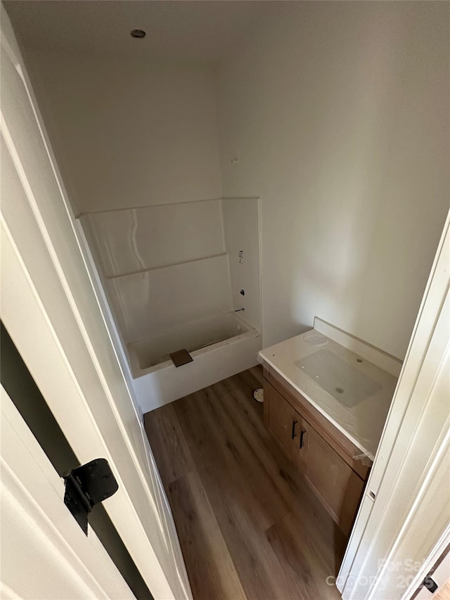 bathroom with a washtub, wood finished floors, and vanity