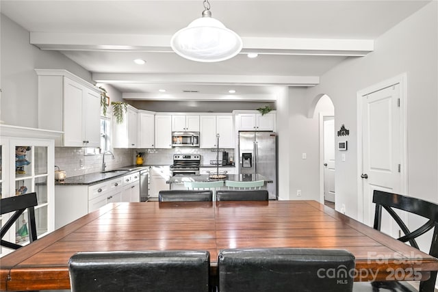 dining space featuring arched walkways, beamed ceiling, and recessed lighting