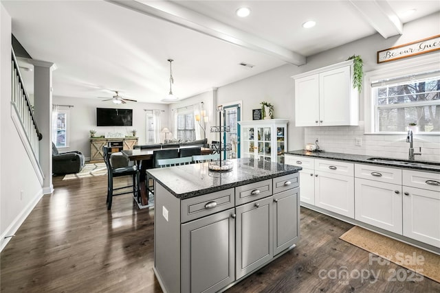 kitchen featuring decorative backsplash, a kitchen island, dark wood-style flooring, beamed ceiling, and a sink