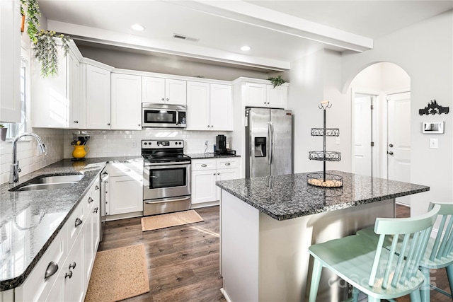 kitchen featuring arched walkways, stainless steel appliances, visible vents, a sink, and a kitchen breakfast bar