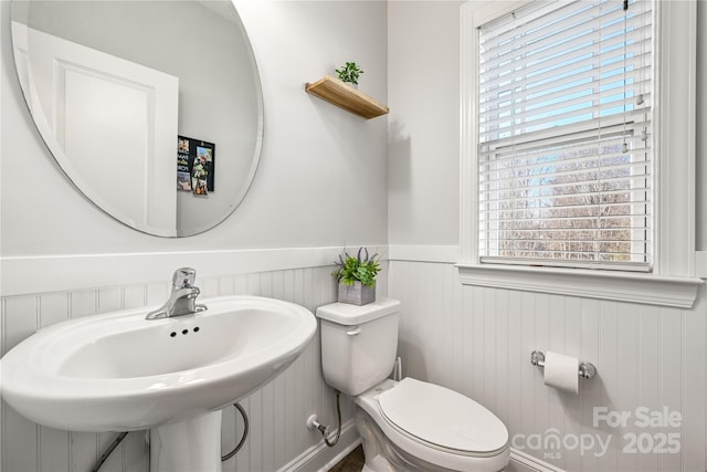 half bathroom featuring toilet, a sink, and wainscoting