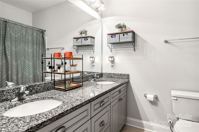 bathroom featuring toilet, double vanity, baseboards, and a sink