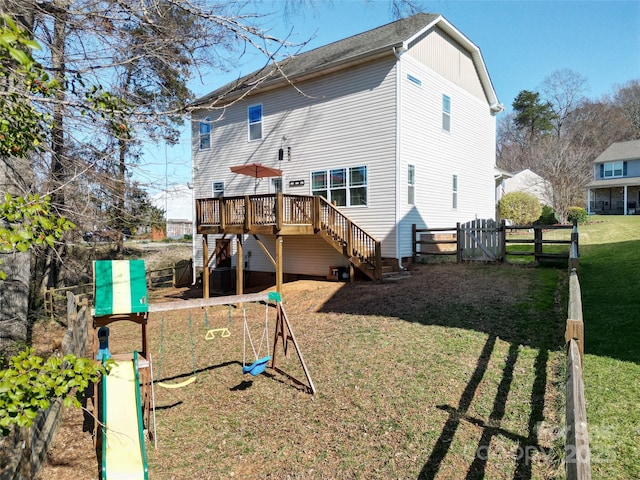 rear view of property featuring a playground, a lawn, fence, a deck, and stairs