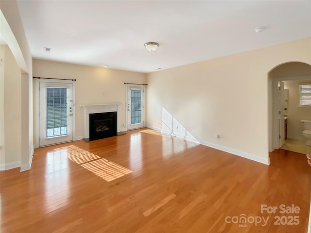 unfurnished living room with arched walkways, a fireplace, light wood-style flooring, and baseboards