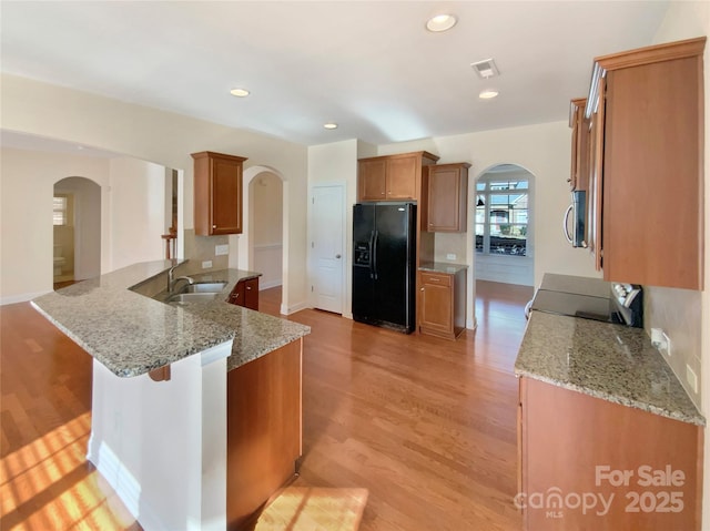 kitchen with electric range, arched walkways, brown cabinetry, black fridge with ice dispenser, and stainless steel microwave