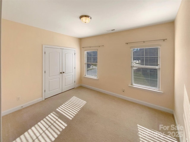 unfurnished bedroom featuring carpet floors, visible vents, baseboards, and a closet