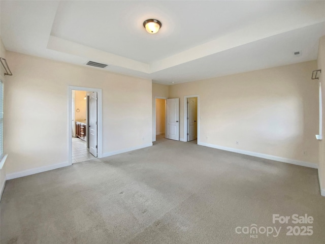 empty room featuring light carpet, baseboards, visible vents, and a tray ceiling