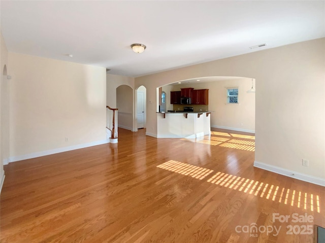 unfurnished living room featuring arched walkways, visible vents, light wood-style floors, baseboards, and stairs