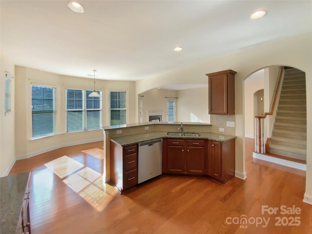 kitchen featuring light wood-type flooring, dark stone counters, dishwasher, and a sink