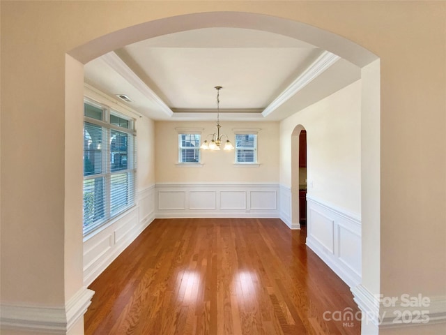 unfurnished dining area with a chandelier, a decorative wall, wood finished floors, visible vents, and a tray ceiling