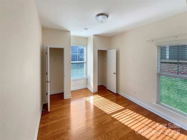 unfurnished bedroom with multiple closets, visible vents, baseboards, and wood finished floors