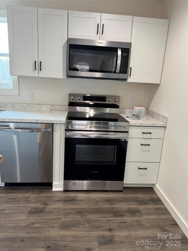 kitchen featuring light stone counters, stainless steel appliances, dark wood-type flooring, baseboards, and white cabinets