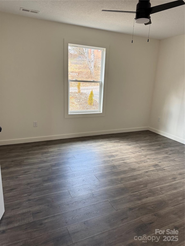 spare room featuring baseboards, a textured ceiling, visible vents, and dark wood-style flooring