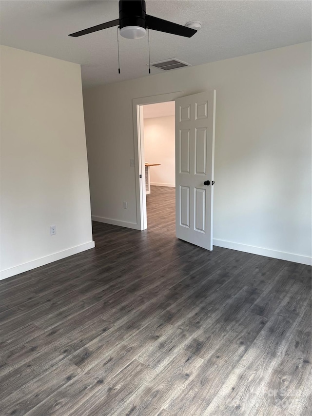 unfurnished room featuring dark wood-type flooring, a ceiling fan, visible vents, and baseboards