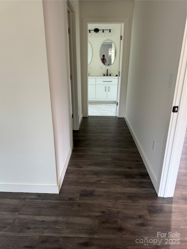 corridor with baseboards, dark wood finished floors, and a sink