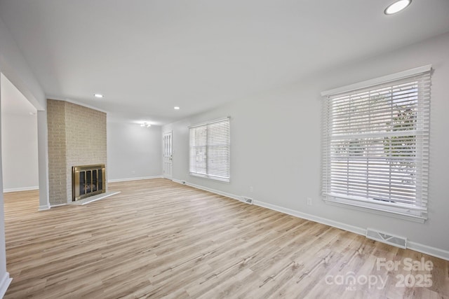 unfurnished living room featuring visible vents, a fireplace, light wood-style flooring, and baseboards