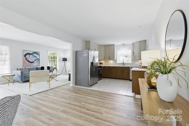 kitchen featuring light countertops, stainless steel appliances, tasteful backsplash, a sink, and light wood-type flooring