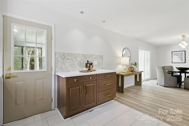 kitchen featuring light countertops, tasteful backsplash, a chandelier, visible vents, and light wood-style flooring