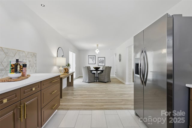 kitchen featuring stainless steel fridge with ice dispenser, light countertops, backsplash, and light tile patterned floors