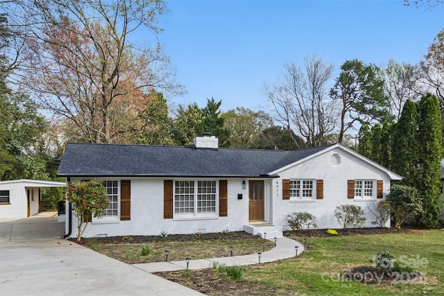 ranch-style house with a chimney, a front yard, brick siding, driveway, and an outbuilding