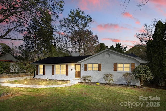 single story home featuring a chimney, brick siding, and a front lawn