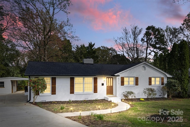 ranch-style house with a chimney, concrete driveway, a front yard, brick siding, and an outdoor structure