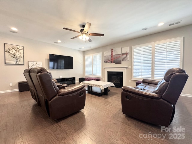 living room featuring baseboards, visible vents, a ceiling fan, a glass covered fireplace, and wood finished floors