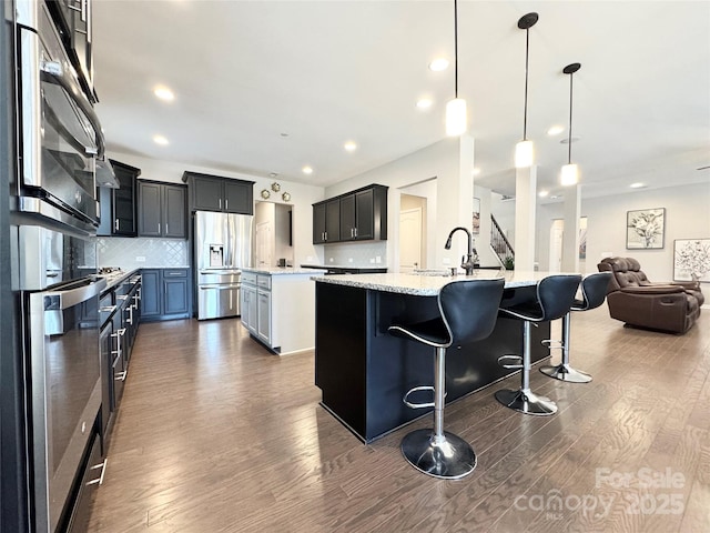 kitchen featuring stainless steel fridge, a kitchen island with sink, open floor plan, and dark wood finished floors