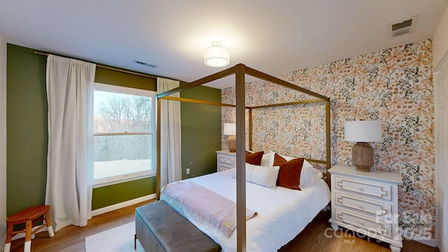 bedroom with visible vents, wallpapered walls, baseboards, and wood finished floors